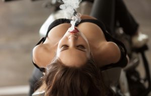 Young sexy woman sitting on motorcycle and smoking ( vaping ) e-cigarette.